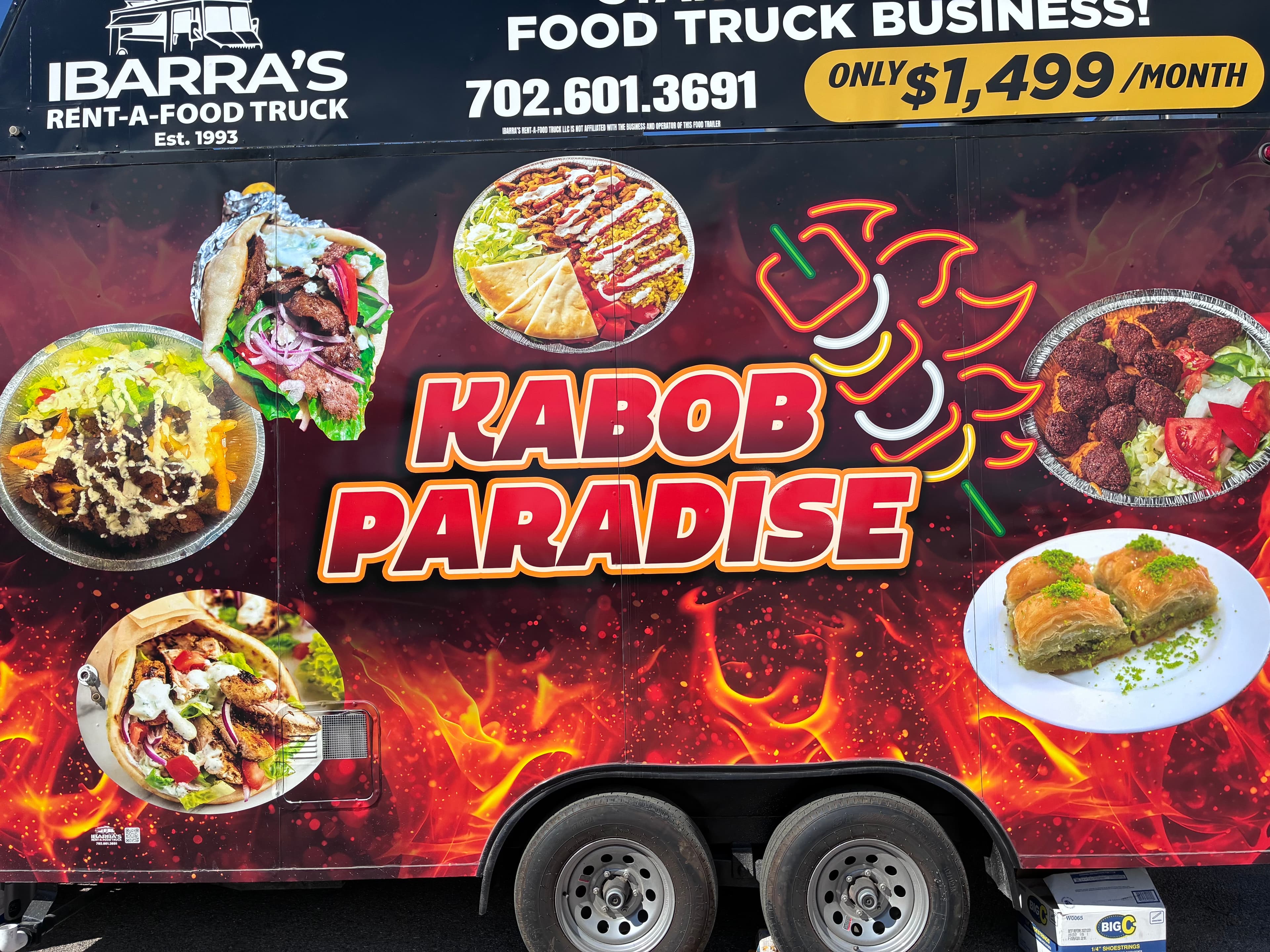 Side of a Kabob Paradise food truck showing Mediterranean dishes against a fiery background.